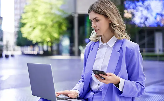 kobieta pracuje na laptopie, trzymając telefon w ręku