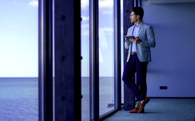 man holding tablet, looking out of the window in the office