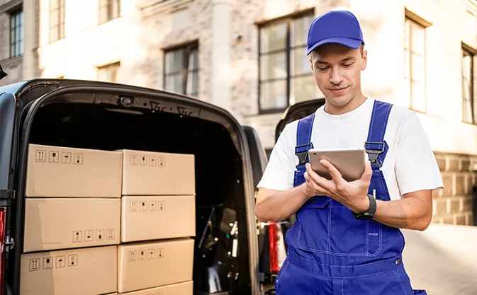 a courier with a tablet standing next to a delivery van