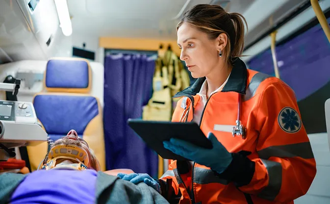 a field worker, a paramedic using a tablet to check on a patient in an ambulance